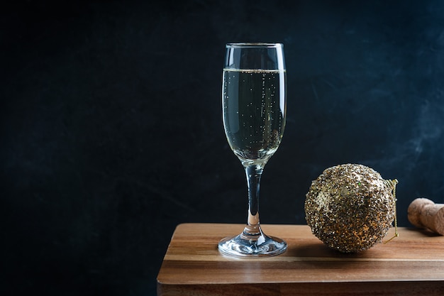 Flute bicchiere di champagne frizzante secco con palla di Natale scintillante dorata sul tavolo di legno scuro