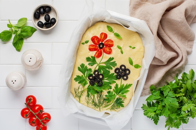 Focaccia ai fiori fatta in casa. Focaccia cruda decorata in modo creativo con verdure su carta forno. Pasta a lievitazione naturale. Pane italiano decorato. Vista dall'alto.