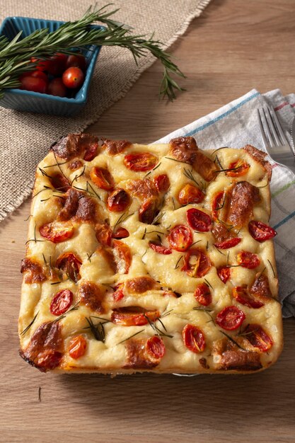 Focaccia al rosmarino, olio d'oliva e pomodoro su tavola di legno.