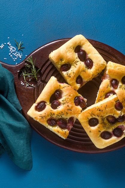 Focaccia con uva rossa su un tavolo blu.