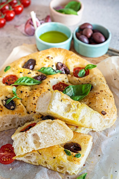 Focaccia di focaccia fresca italiana con pomodori, olive, aglio ed erbe aromatiche su sfondo chiaro.