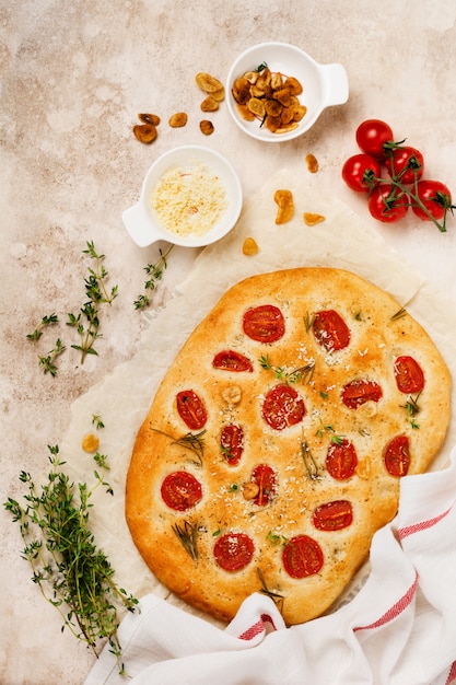 Focaccia italiana con con pomodori, parmigiano e rosmarino su sfondo marrone chiaro