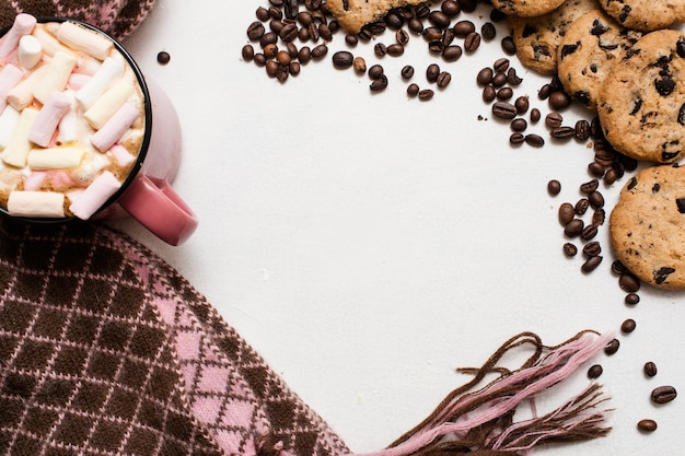 Focaccina al cioccolato e tazza di latte con marshmallow, sciarpa calda e accogliente nelle vicinanze, vista dall'alto, spazio libero al centro. Deliziosa mattina fredda con biscotti e bevande calde