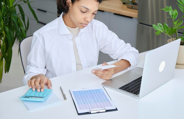 Focalizzato giovane donna afroamericana in occhiali guardando attraverso documenti cartacei gestione affari affari riassumendo le tasse pianificazione investimenti futuri contabilità da solo