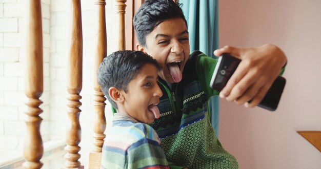 Focalizzazione superficiale di due fratelli indiani che fanno le facce mentre si fanno dei selfie in casa