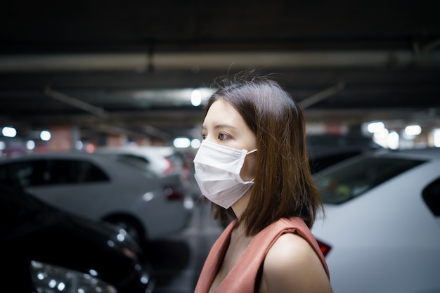 Focolaio diffondente Covid-19. Donna nella mascherina protettiva medica ad un parcheggio. Paura del coronavirus.