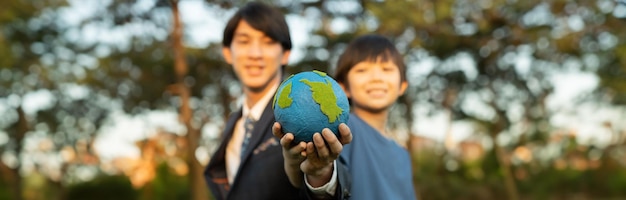 Focus panorama Terra con sfocatura ragazzo asiatico e uomo d'affari che tengono insieme il globo come concetto della Giornata della Terra Responsabilità sociale aziendale per rendere l'ambiente più verde per la generazione futura sostenibile Gyre