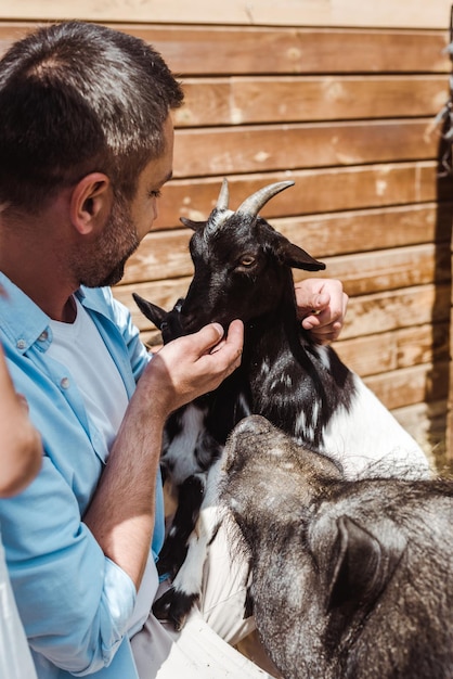 Focus selettivo dell'uomo allegro che tocca la capra vicino al cinghiale nello zoo