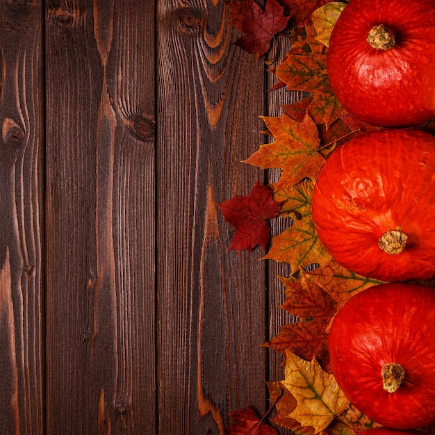 Fogli di autunno con le zucche su una tabella di legno