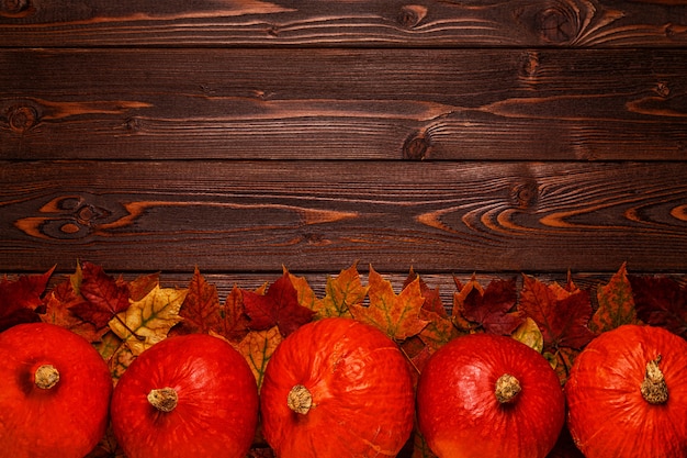 Fogli di autunno con le zucche su una tabella di legno