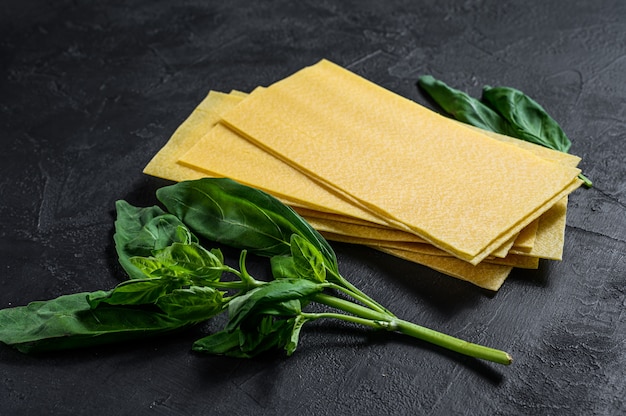 Fogli di lasagne crude e foglie di basilico. Sfondo nero. Vista dall'alto. Spazio per il testo