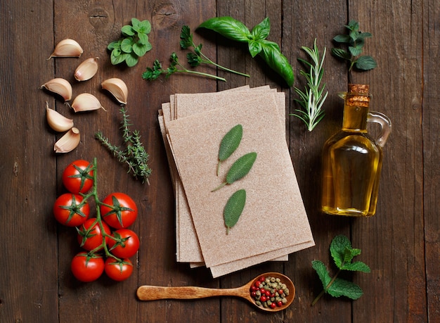 Fogli di lasagne integrali, verdure ed erbe sulla tavola di legno