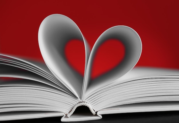 Fogli di libro curvati a forma di cuore su sfondo rosso sfocato