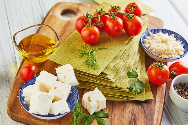 Fogli per lasagne con spinaci e ingredienti: pomodorini, formaggio, burro, peperoni ed erbe aromatiche.
