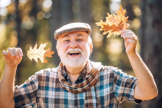 Foglie autunnali cadute sparse per terra uomo anziano sorridente all'aperto in natura nonno havi...