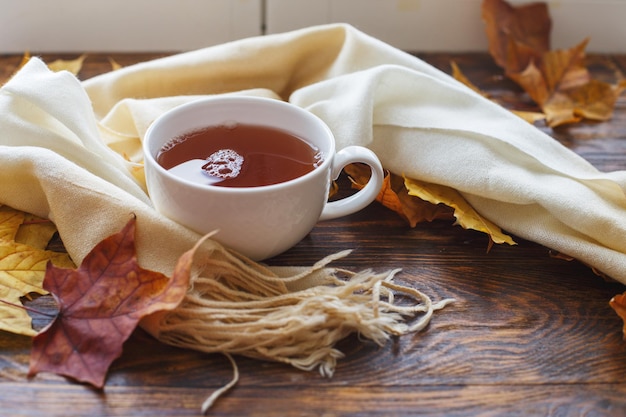 Foglie d'autunno con una tazza di tè o caffè accanto a una sciarpa su uno sfondo di legno con spazio per la copia