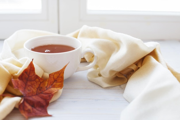 Foglie d'autunno con una tazza di tè o caffè accanto a una sciarpa su uno sfondo di legno con spazio per la copia