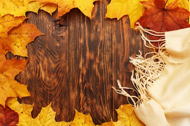 Foglie d'autunno su fondo in legno con una sciarpa beige Cornice di foglie d'autunno