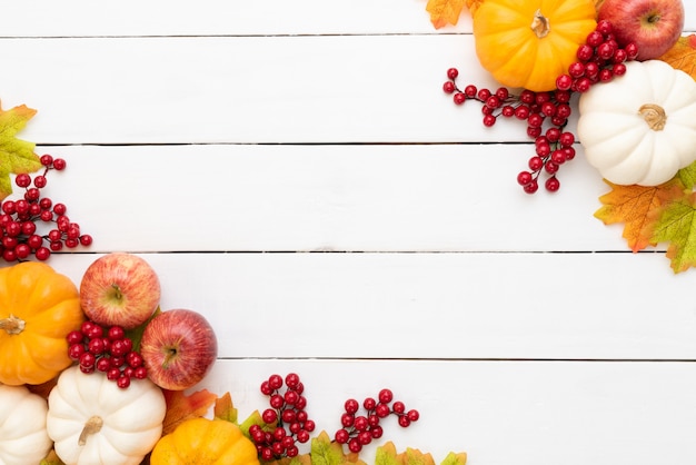 Foglie di acero di autunno con la zucca e le bacche rosse su fondo di legno.