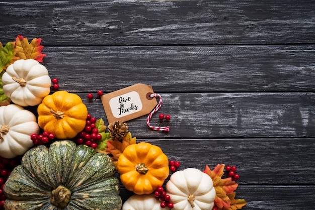 Foglie di acero di autunno con la zucca e le bacche rosse su vecchio fondo di legno. Ringraziamento