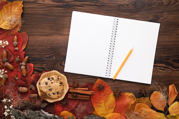 Foglie di autunno, biscotti e taccuino di carta su legno