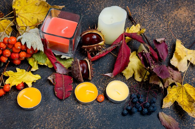 Foglie di autunno, castagne, candele su uno sfondo scuro