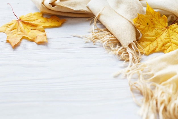 Foglie di autunno con una sciarpa su un fondo di legno con lo spazio della copia