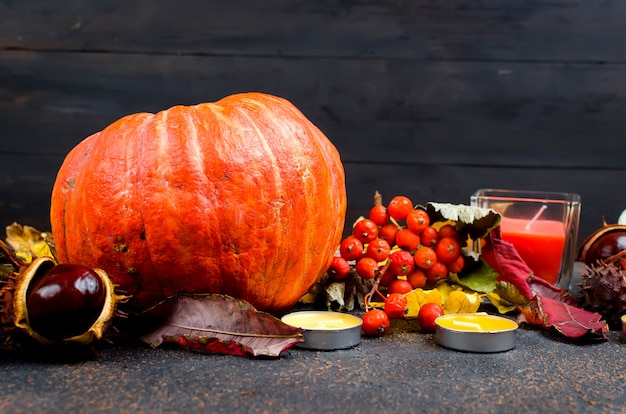 Foglie di autunno, zucca, castagne, candele su una superficie scura