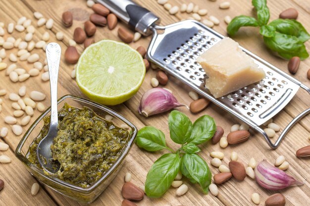 Foglie di basilico, olio d'oliva, parmigiano su grattugia, aglio, pinoli. Cottura al pesto. Vista dall'alto. Sfondo di legno chiaro