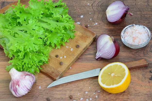 foglie di insalata verde fresca su un tagliere con un coltello, cipolla rossa, limone e aglio
