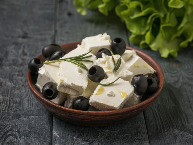 Foglie di lattuga e una ciotola di formaggio feta e olive su un tavolo di legno. Formaggio naturale prodotto con latte di pecora.