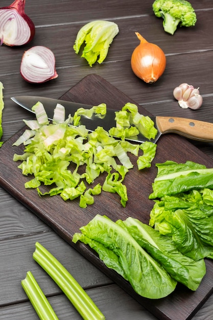 Foglie di lattuga tritate e coltello sul tagliere Cipolla, aglio e gambi di sedano sul tavolo