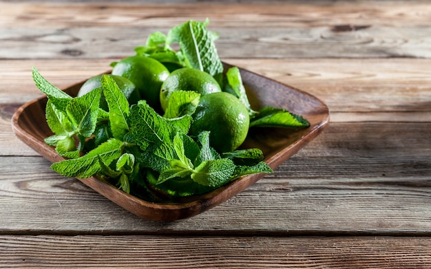 Foglie di menta fresca e calce verdi in un piatto di legno su un fondo di legno.