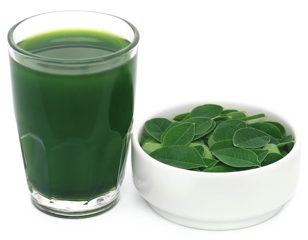 Foglie di Moringa con estratto in un bicchiere su sfondo bianco