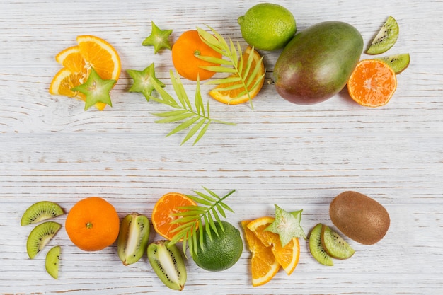 Foglie di palma verdi e fette tropicali fresche di frutta sulla tavola di legno bianca