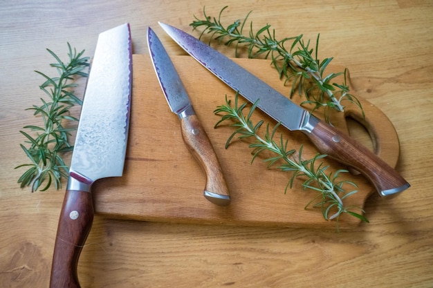 Foglie di rosmarino su una tavola di legno in cucina accanto a un coltello d'acciaio damash