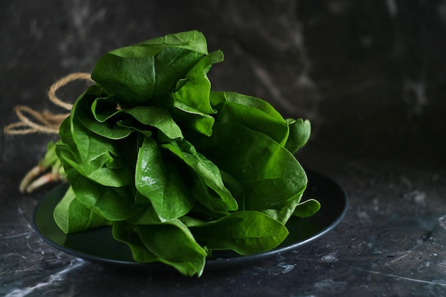 Foglie di spinaci freschi verdi giacciono in un piatto su un tavolo di marmo