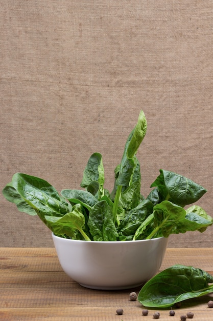 Foglie di spinaci in ciotola di ceramica. Pimento e una foglia di spinaci sul tavolo. Fondo in legno. Copia spazio