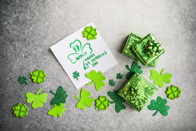 Foglie di trifoglio decorativo, scatola regalo verde, monete su sfondo di pietra, piatto laici. Celebrazione del giorno di San Patrizio. Carta felice giorno di San Patrizio