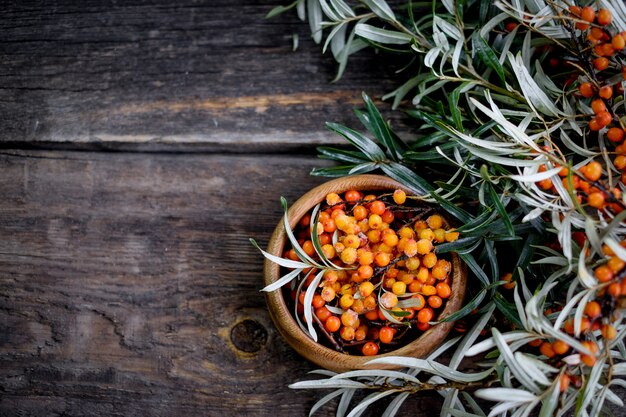 Foglie e bacche dell'olivello spinoso arancio sulla tavola di legno