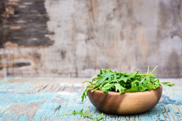 Foglie fresche di rucola in una ciotola di legno su un tavolo di legno. Copia spazio