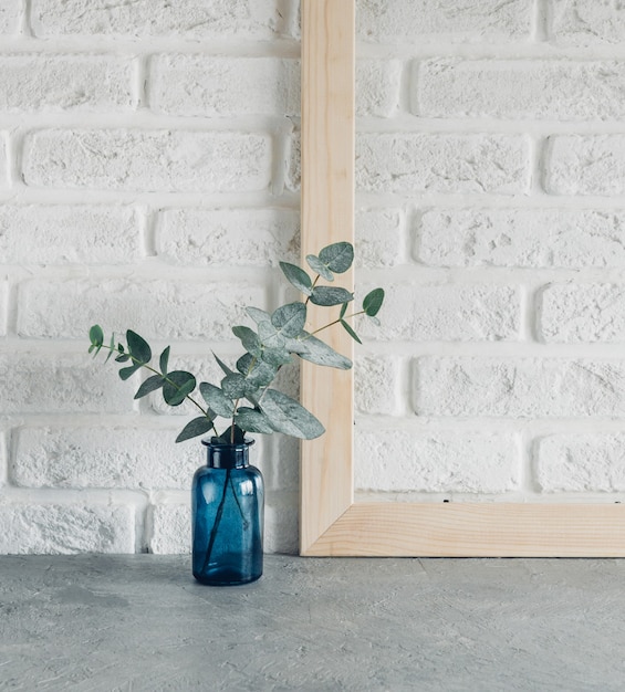 Foglie verdi di eucalipto in un vaso blu e cornice in legno contro un muro di mattoni bianchi Minimalismo in stile scandinavo.