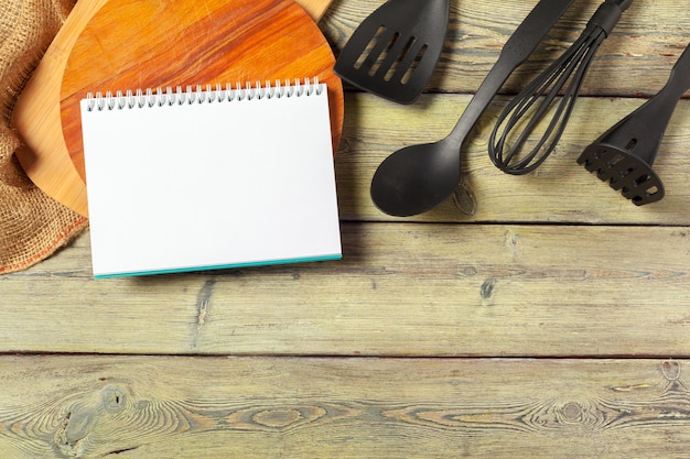 Foglio bianco degli utensili aperti del blocco note e della cucina sul tavolo con la tovaglia