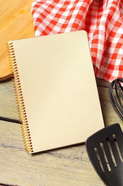 Foglio bianco di blocco note aperto e utensili da cucina sul tavolo con tovaglia, spazio copia