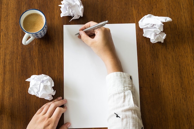 Foglio bianco di carta e penna sulla scrivania in legno luminoso con le mani di una persona