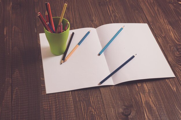 Foglio di carta bianco con un bicchiere con matite e matite sono anche su una carta sul tavolo