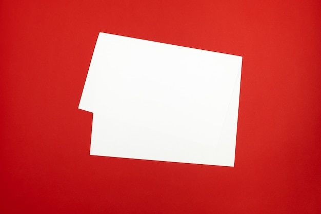 Foglio di carta bianco su sfondo rosso brillante. Vista superiore del libro bianco piegato posa sul piano del tavolo colorato vivido