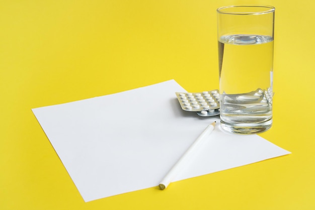 Foglio di carta bianco vuoto con una matita accanto a un bicchiere d'acqua e pillole