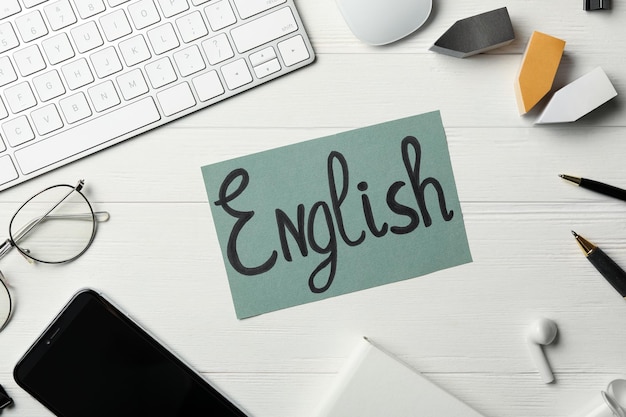 Foglio di carta con parola tastiera INGLESE smartphone e cancelleria su fondo di legno bianco piatto