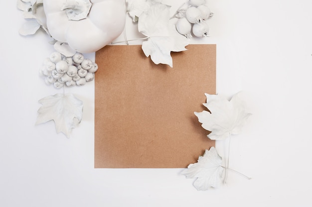 Foglio di carta Kraft, zucca bianca, bacche e foglie su uno sfondo bianco.